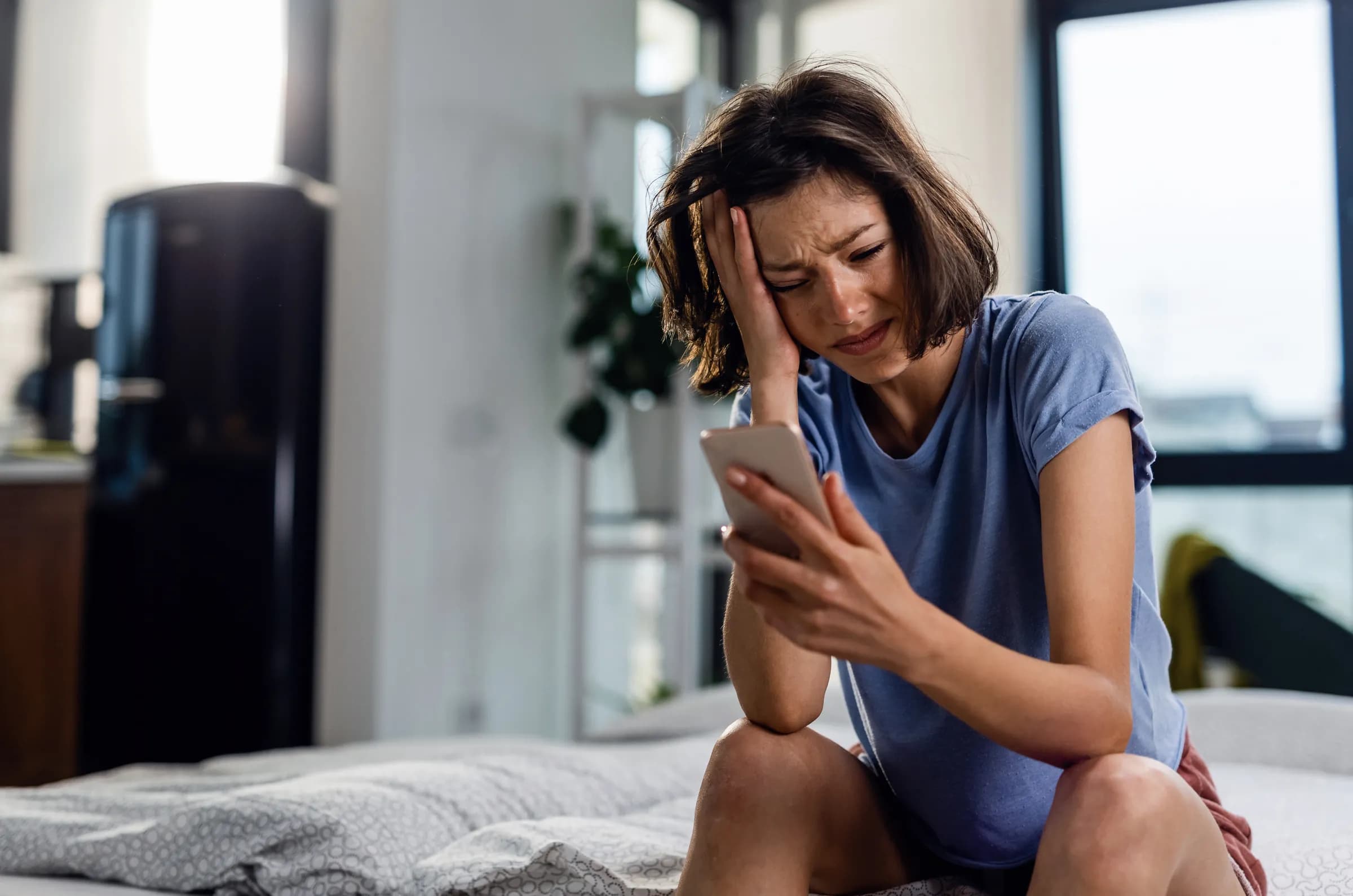 Worried woman sitting on a bed looking at a phone