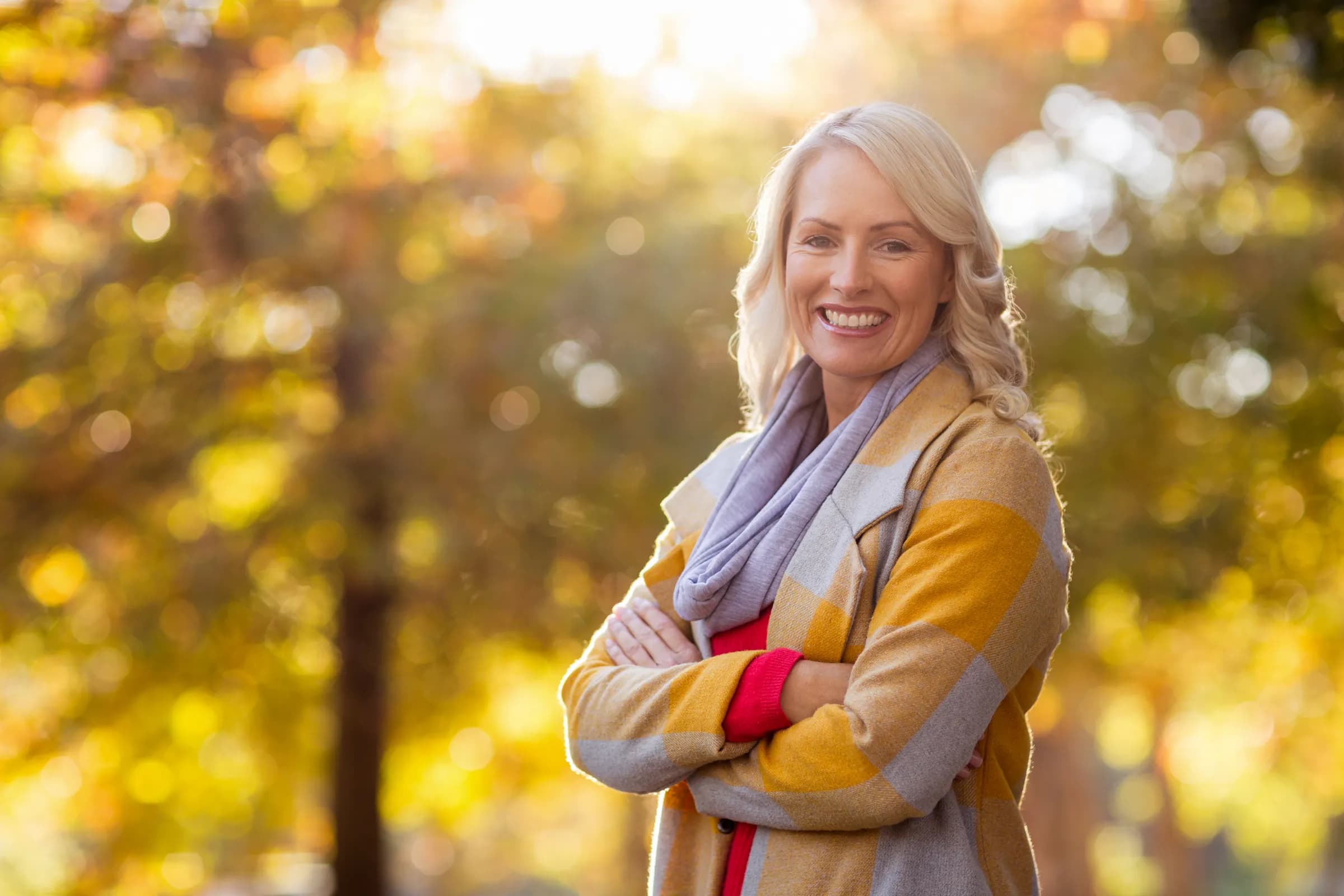 Smiling woman outdoors in autumn light, wearing a yellow checkered coat